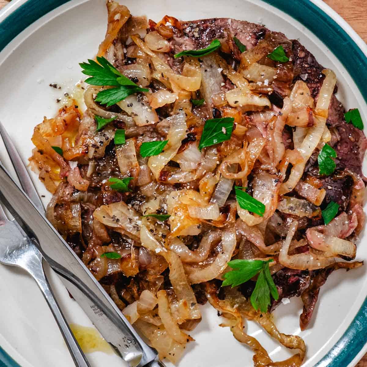 Baked beef liver and onions plated with caramelized onions and fresh parsley on a white dish, easy high protein dinner recipe