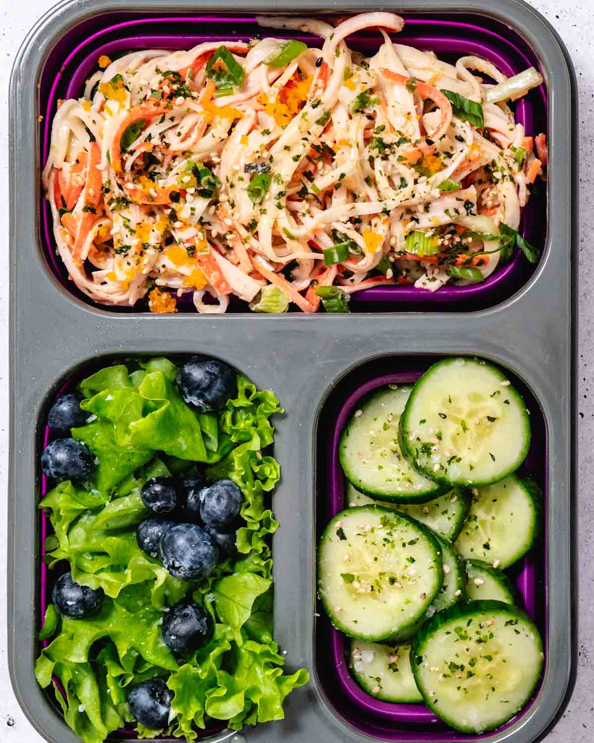 Kani salad bento box with shredded imitation crab, cucumber slices, and mixed greens, topped with sesame seeds and fish roe.