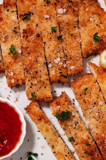 sliced crispy chicken cutlet with lemon wedges and ketchup
