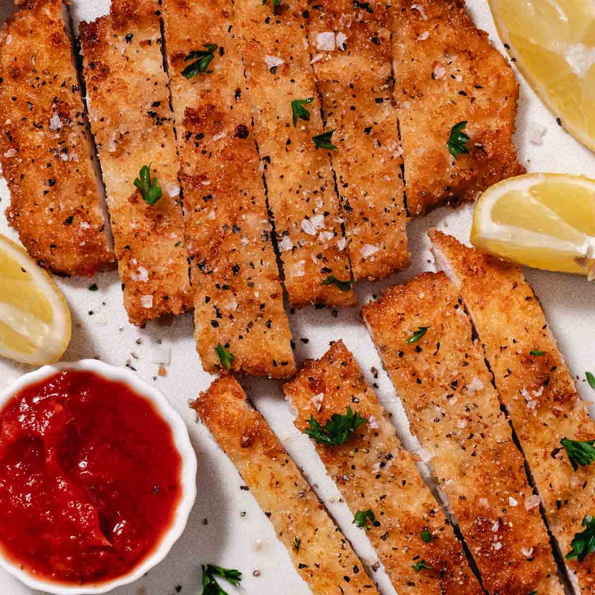 sliced crispy chicken cutlet with lemon wedges and ketchup