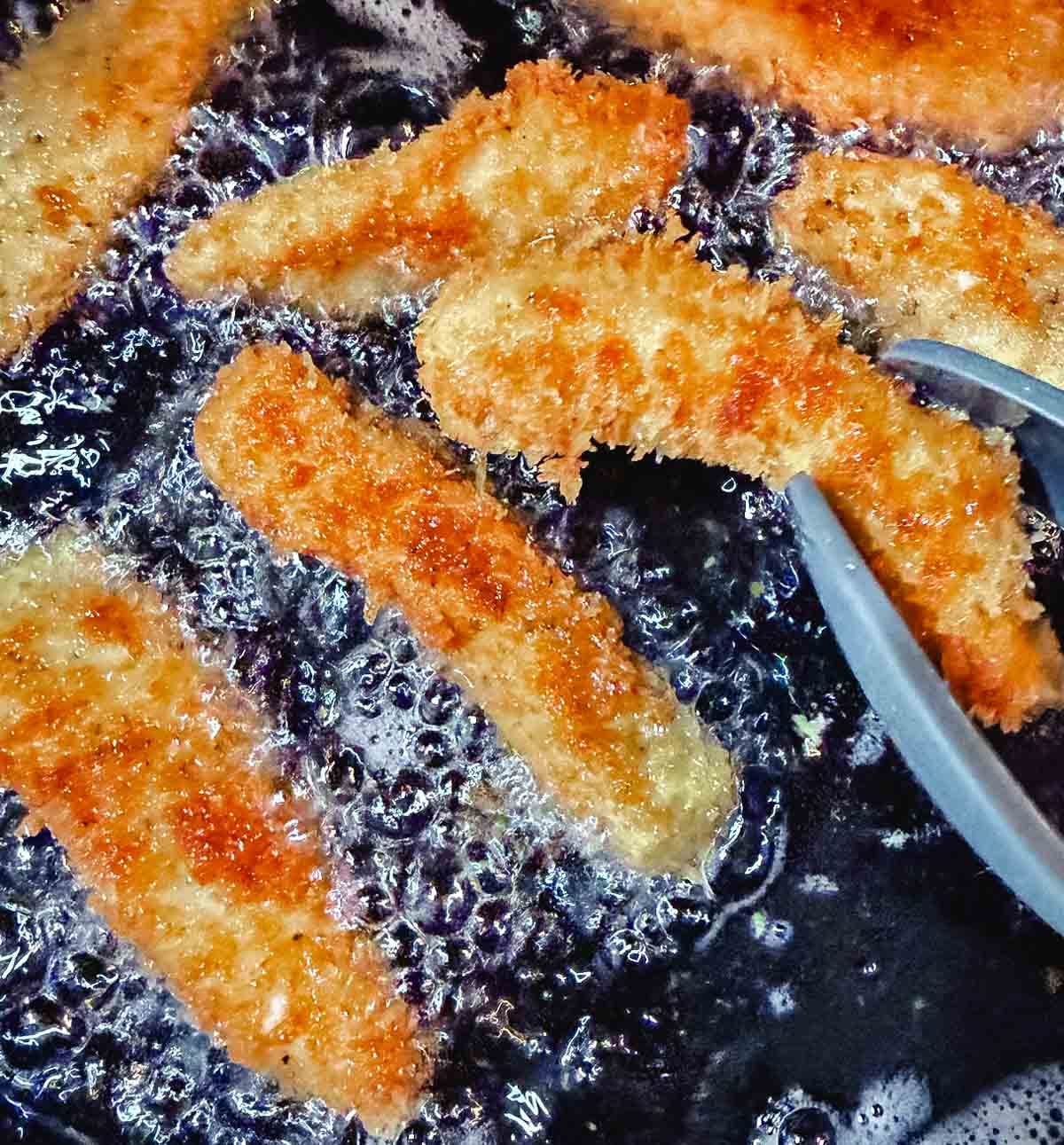 Panko chicken strips frying in hot oil in a skillet until golden brown