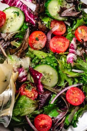 Mixed garden salad with cucumbers, cherry tomatoes, and red onion as lemon Dijon dressing is poured over fresh greens