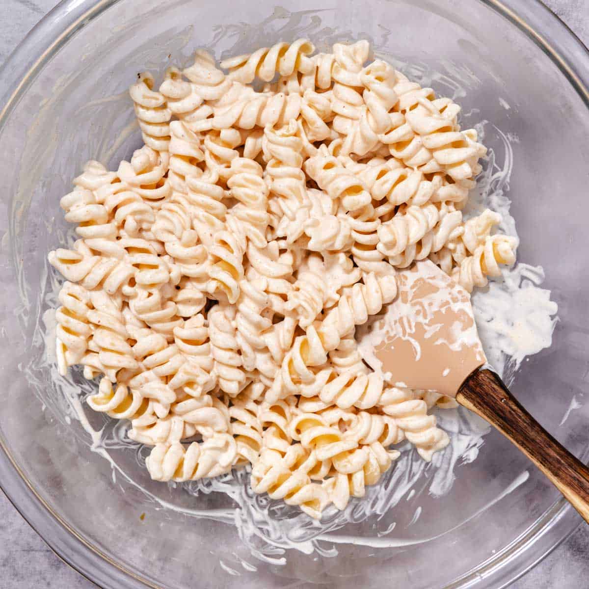 Fusilli pasta coated in creamy dressing for crab meat pasta salad in a mixing bowl.