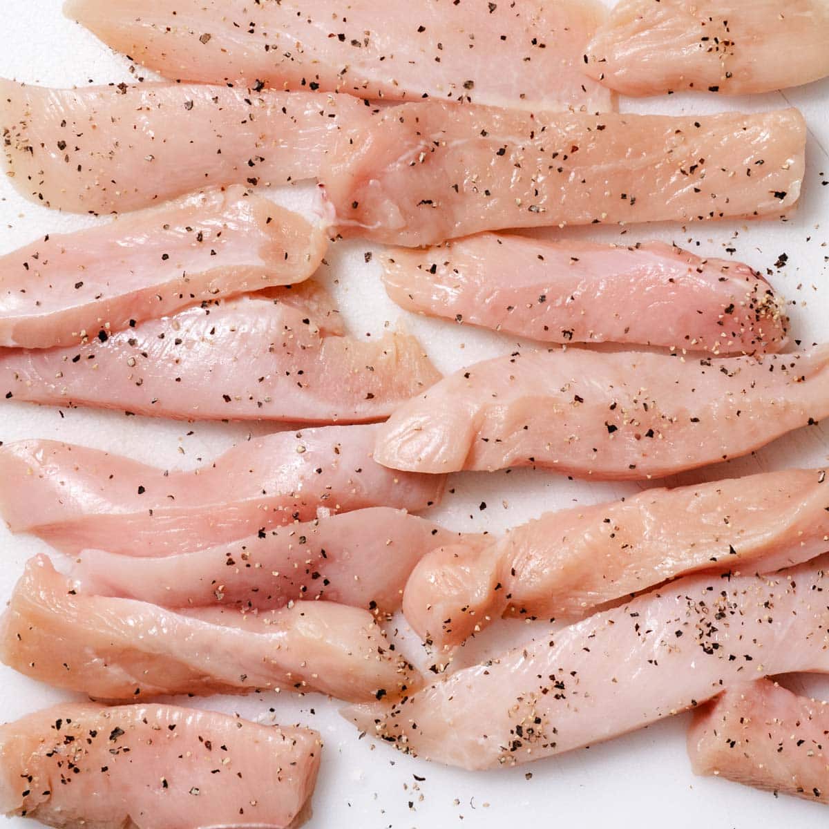 Raw chicken breast strips seasoned with salt and black pepper.