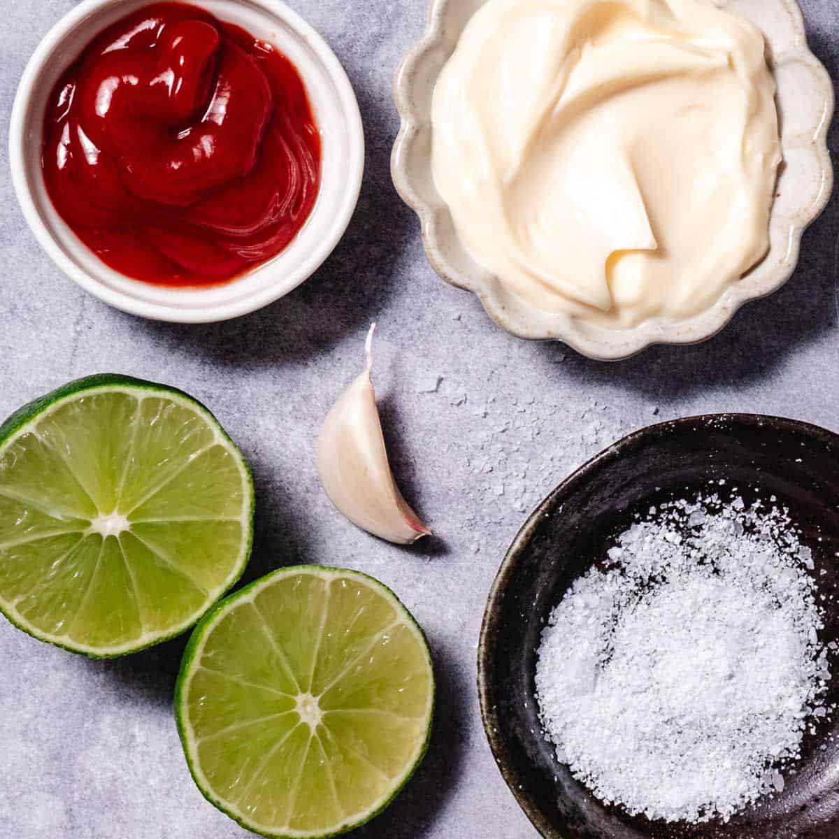 mayo ketchup sauce ingredients with mayonnaise, ketchup, lime, garlic, and salt on a countertop