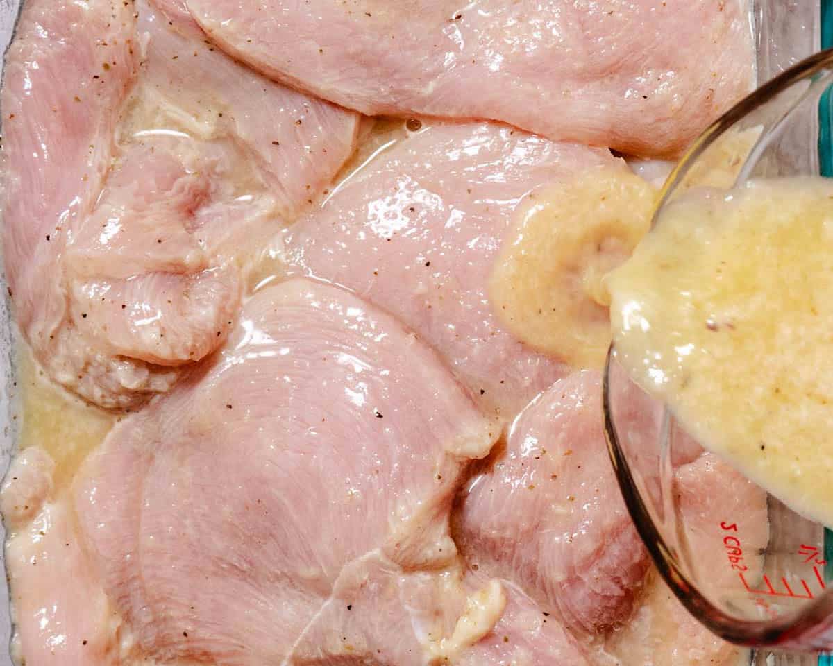 Raw chicken marinating in mojo sauce with garlic, citrus, and spices in a glass dish