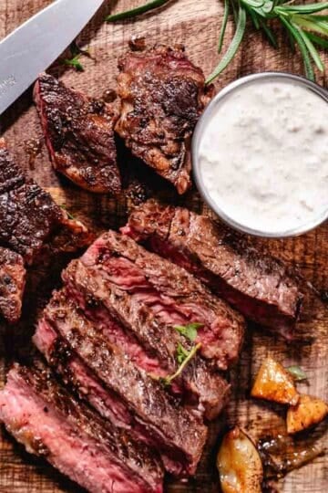 Pan fried rib eye steak sliced on a plate with butter and garlic, showing a juicy center and seared crust with a side of horseradish sauce