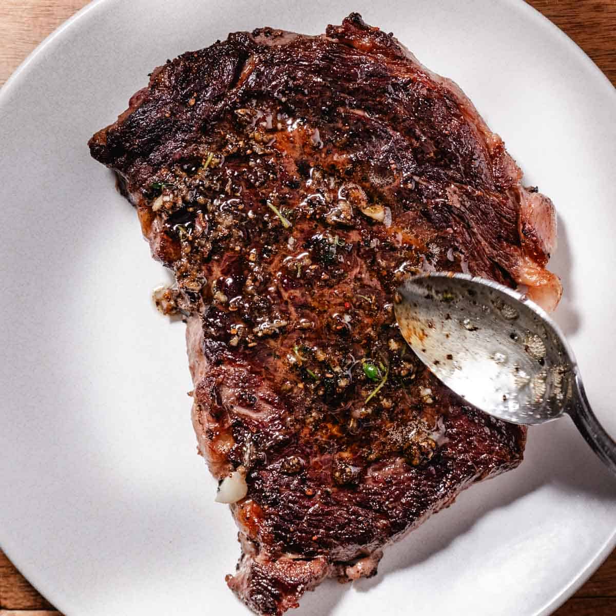 spooning garlic butter sauce over boneless rib steak