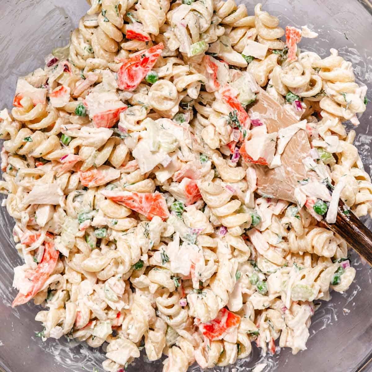 Crab meat pasta salad mixed with creamy dressing, celery, peas, and red onion in a bowl