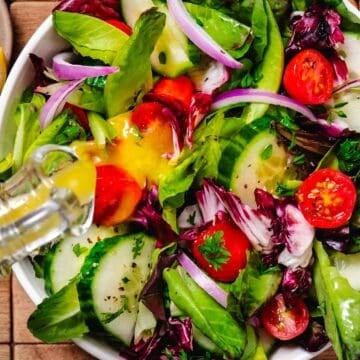 lemon dijon dressing poured over fresh garden salad with cucumbers and tomatoes