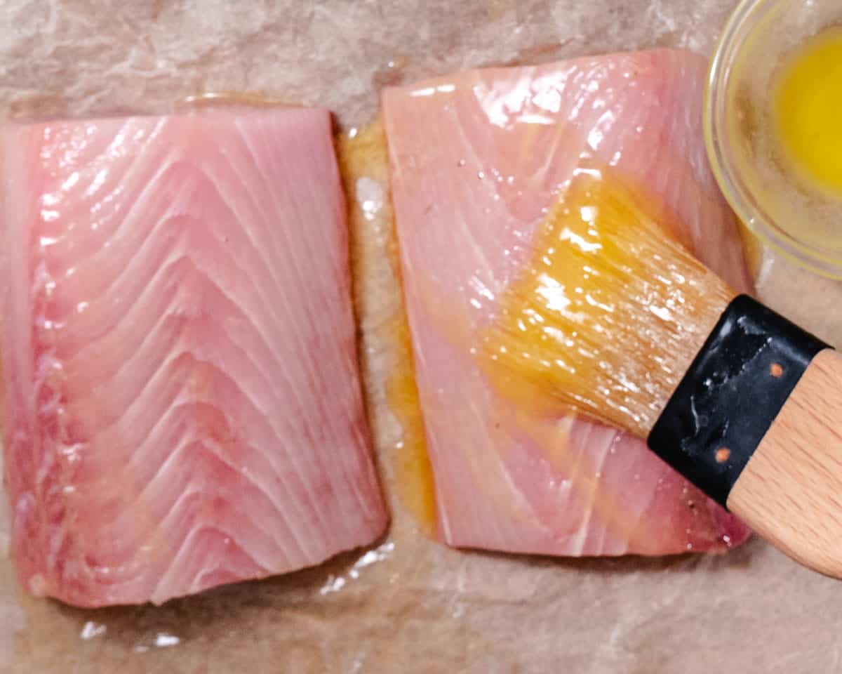Brushing melted butter onto fresh mahi mahi fillets before seasoning