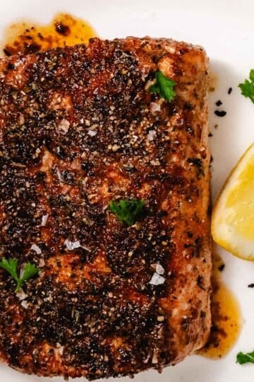 Blackened mahi mahi fillet with lemon and melted butter on a white plate