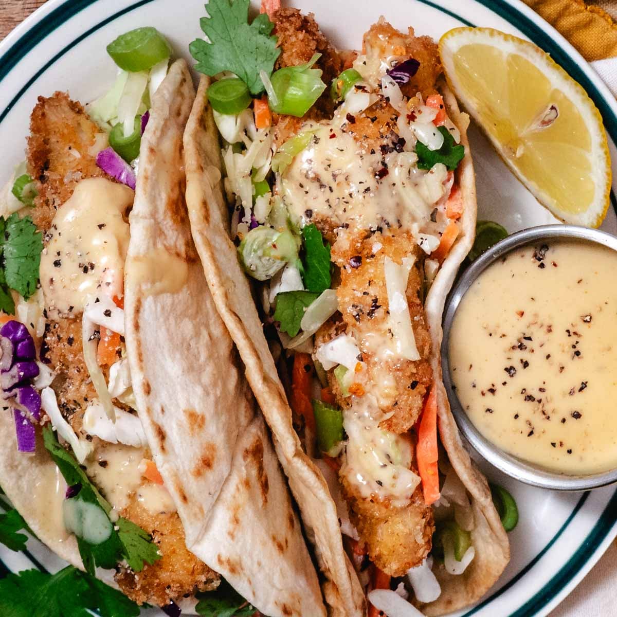 Crispy chicken tortillas topped with coleslaw mix, green onions, and honey mustard sauce served with a lemon wedge and extra dipping sauce.