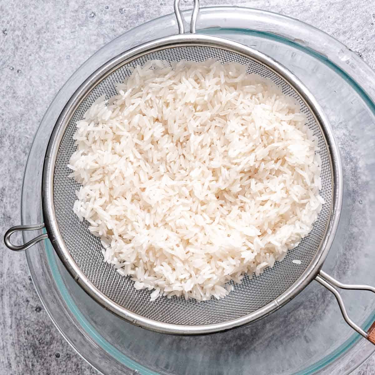 Rinsing jasmine rice for coconut rice in a fine mesh strainer.