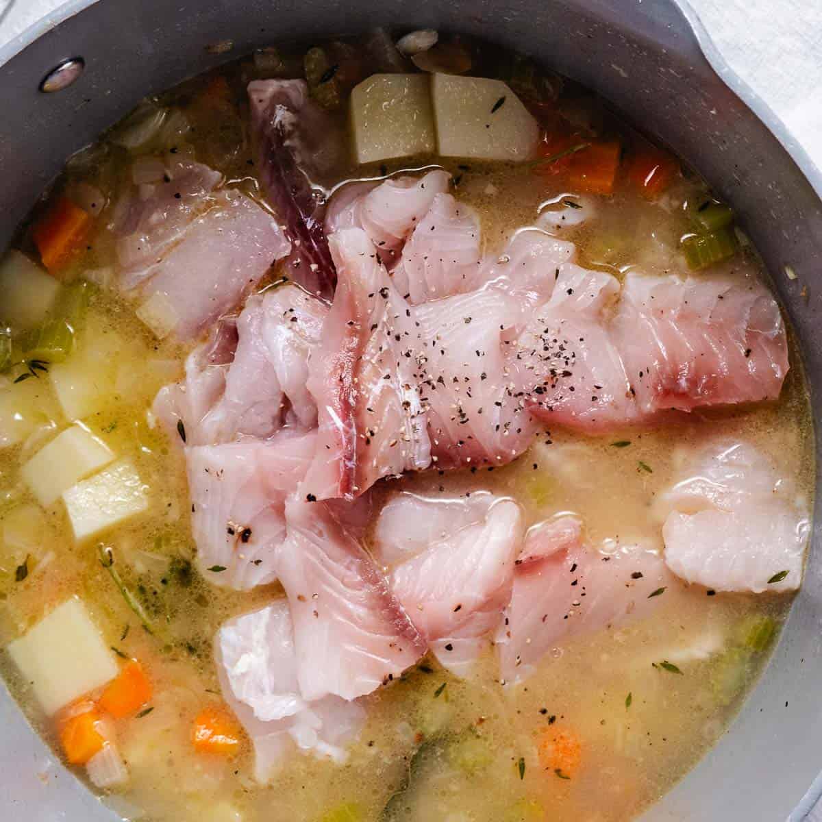 Fresh fish added to fish chowder with potatoes, carrots, celery, and fish stock