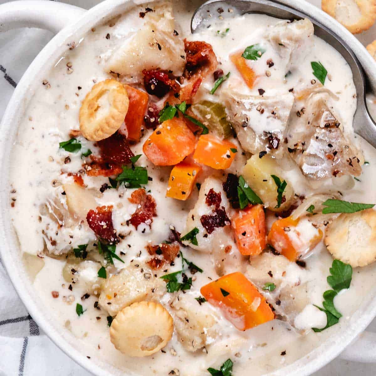 Creamy fish chowder with white fish, potatoes, carrots, bacon, parsley, and oyster crackers