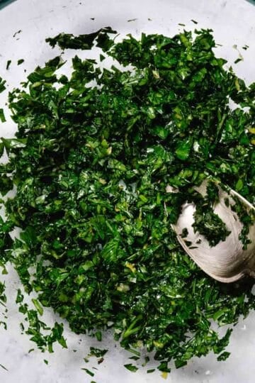 Finished gremolata with parsley, garlic, and lemon zest in a bowl with a spoon ready to serve