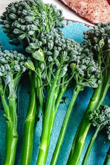 Raw broccolini, also called baby broccoli, on a blue plate before grilling.