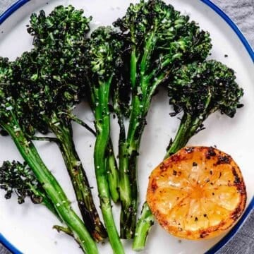 grilled baby broccoli with lemon on white plate.