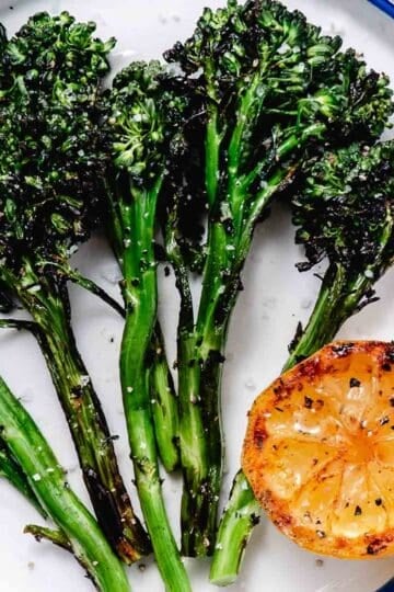 grilled baby broccoli with lemon on white plate.