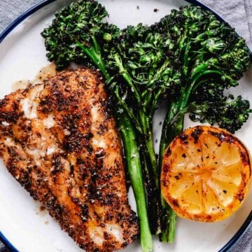 Grilled red snapper fillet with charred baby broccoli and grilled lemon on a white plate with blackened seafood seasoning