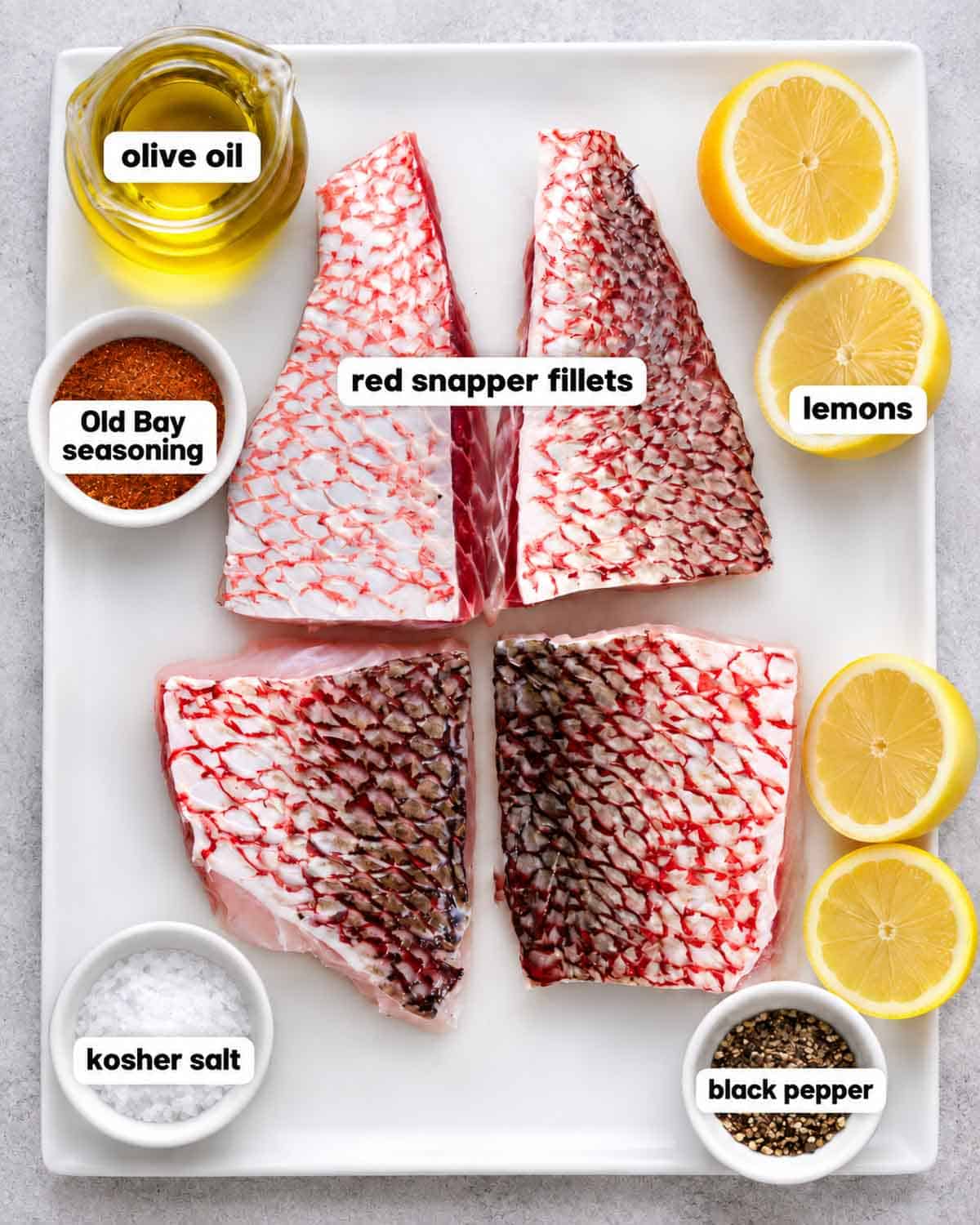 Raw red snapper fillets with olive oil, Old Bay seasoning, kosher salt, black pepper, and lemons.