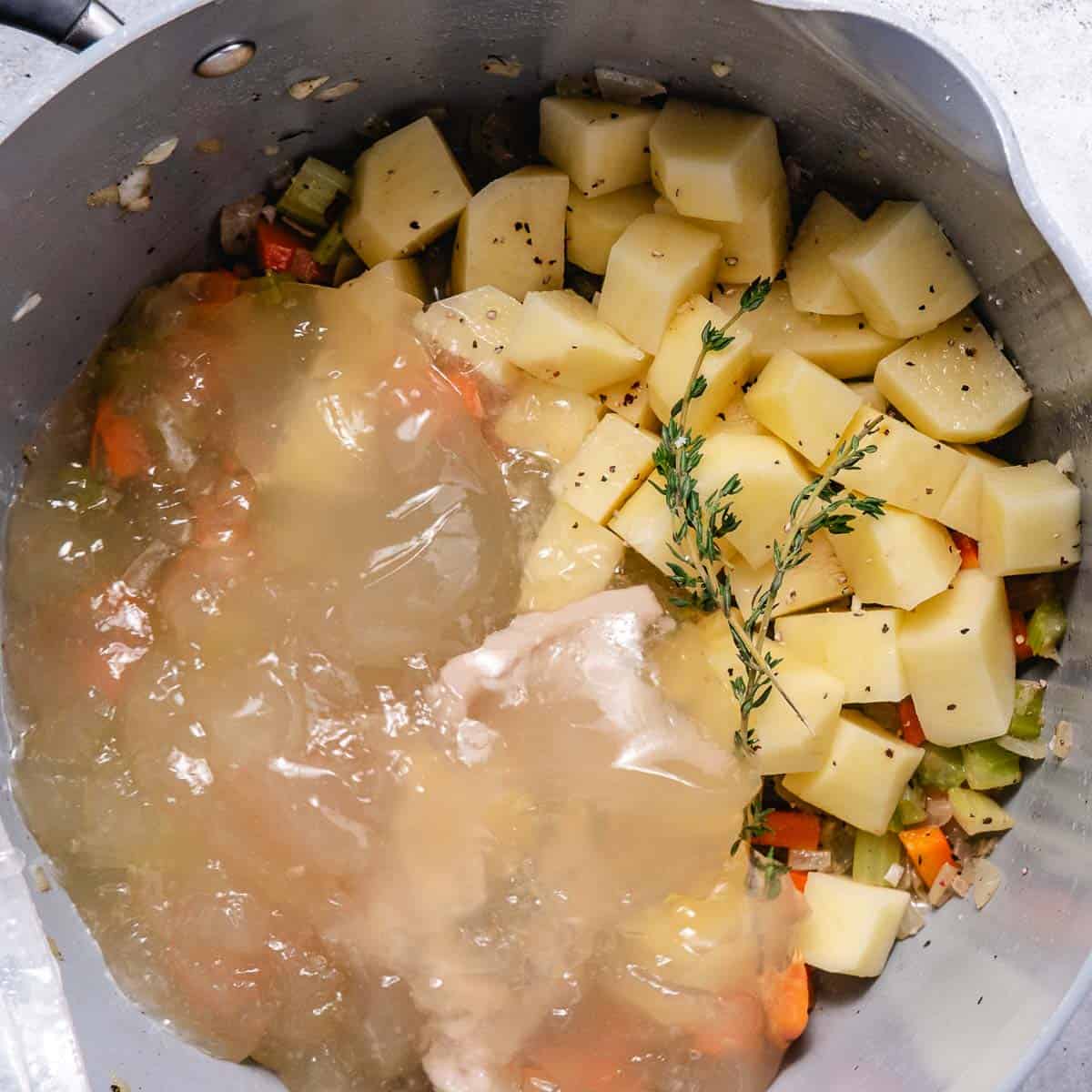 Adding homemade fish stock to potatoes, carrots, celery, onions, and fresh thyme while making fish chowder.