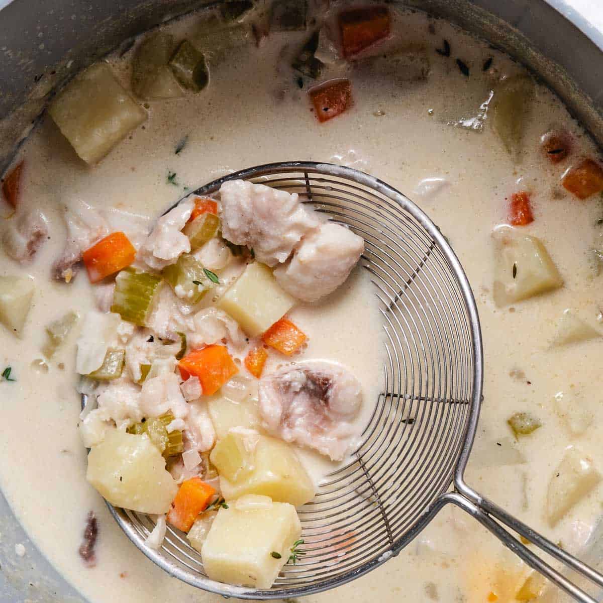Creamy fish chowder with white fish, potatoes, carrots, celery, and fish stock in a soup pot.