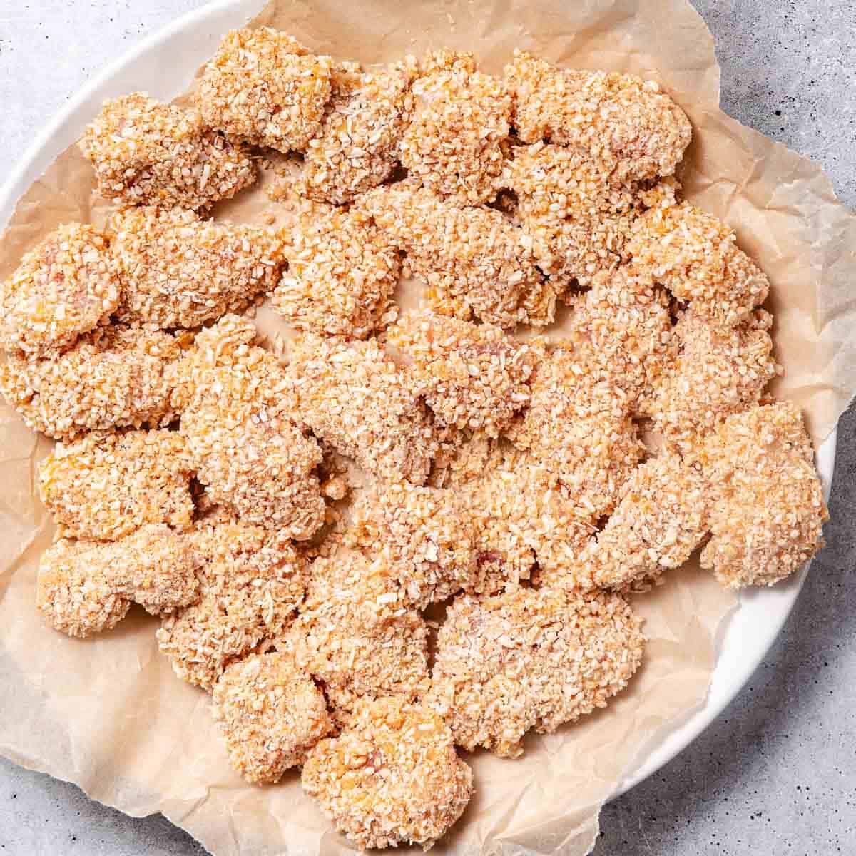 Coconut chicken nuggets coated in gluten-free breadcrumbs and coconut flakes before frying.