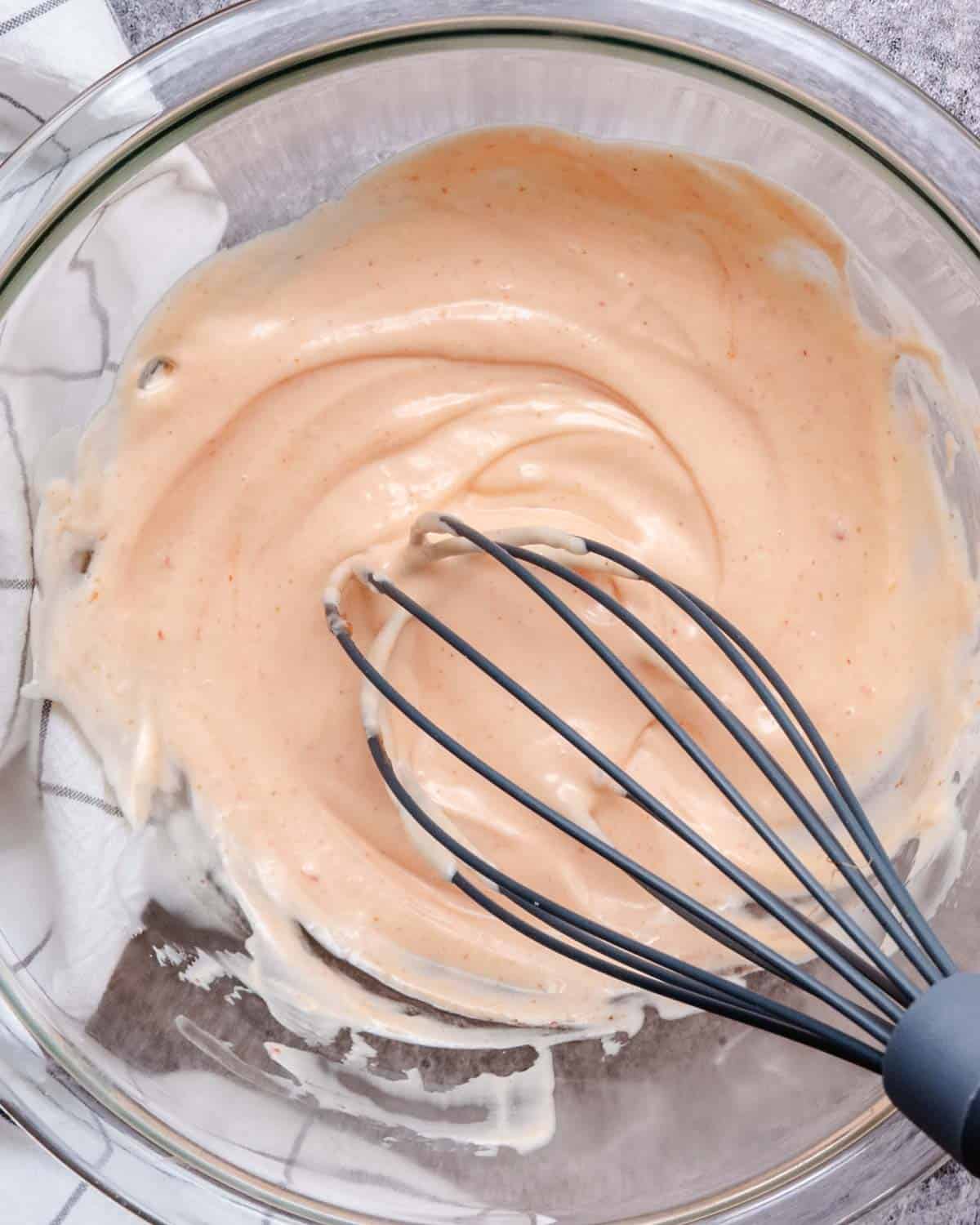 Homemade bang bang sauce mixed in a glass bowl with a whisk