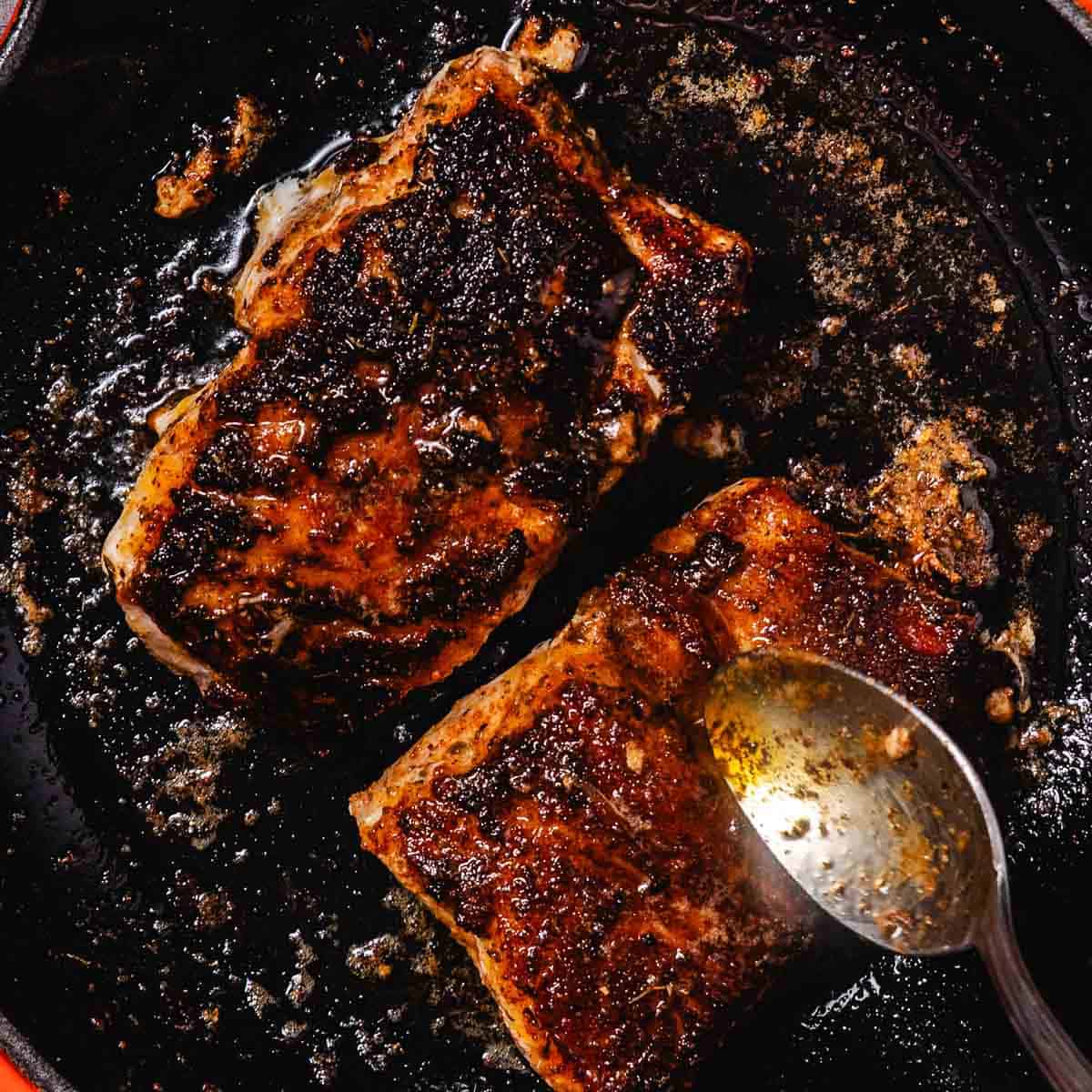 Blackened grouper cooking in a cast iron skillet with melted butter.