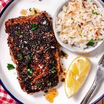 Blackened grouper served on a white plate with coconut rice and lemon.