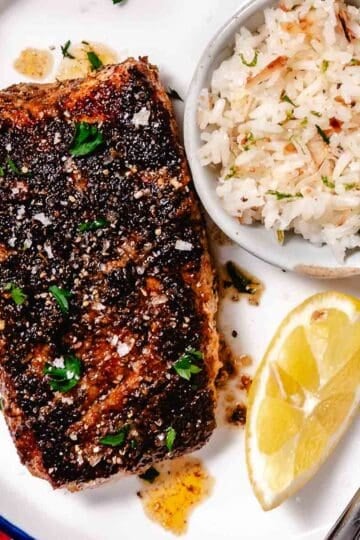 Blackened grouper served on a white plate with coconut rice and lemon.