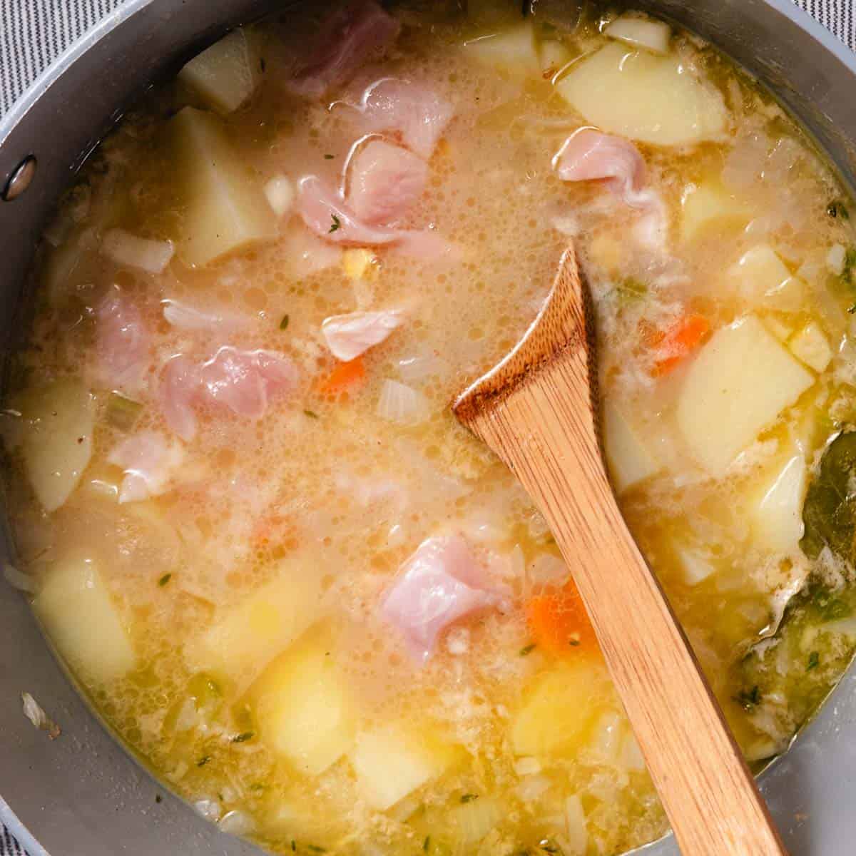 Chicken breast and potatoes simmering in broth with onion, celery, carrots, and thyme for homemade chowder.