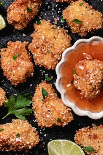 Gluten-free coconut chicken nuggets with sweet chili dipping sauce, lime wedges, and flaky sea salt.
