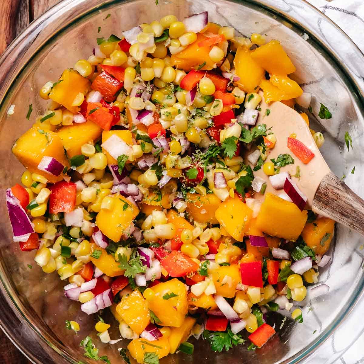 Mixing corn mango salsa in a glass bowl.