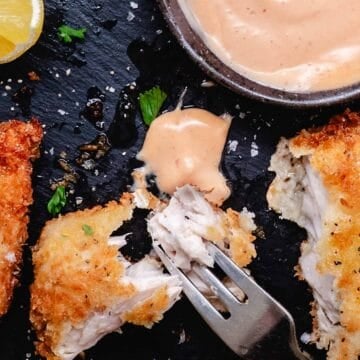 Crispy fried fish pieces with bang bang sauce, lemon, and parsley on a black slate plate