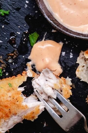 Crispy fried fish pieces with bang bang sauce, lemon, and parsley on a black slate plate