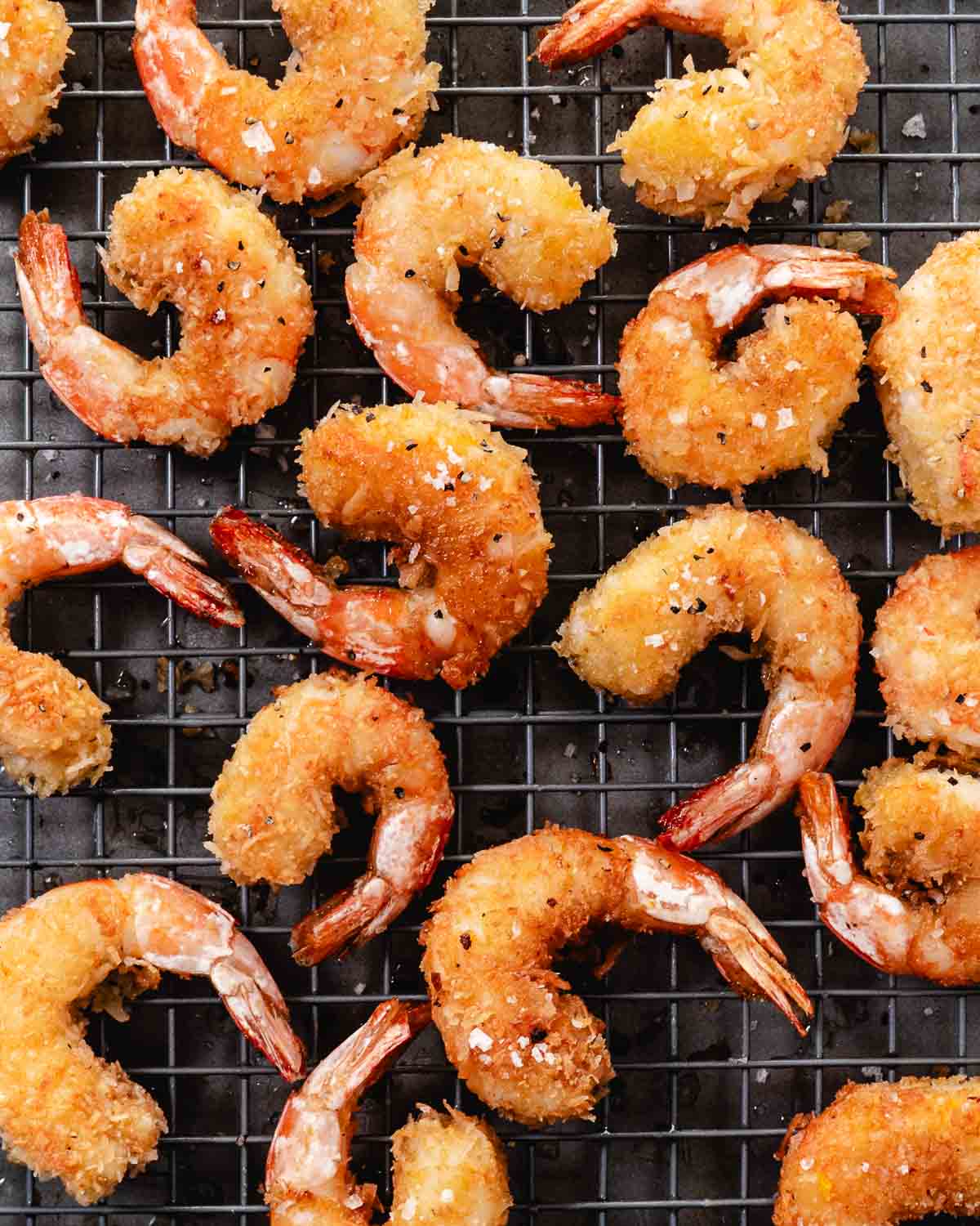 Gluten-free coconut shrimp cooling on a wire rack after frying.