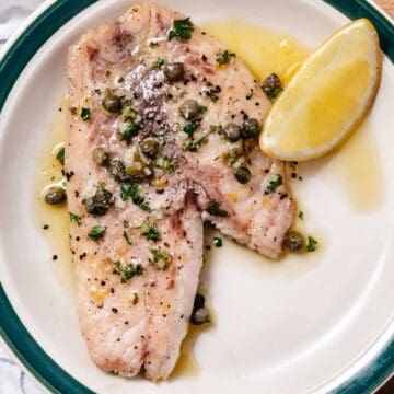 Pan-seared fish topped with lemon butter, capers, garlic, and parsley with a lemon wedge