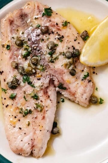 Pan-seared fish topped with lemon butter, capers, garlic, and parsley with a lemon wedge