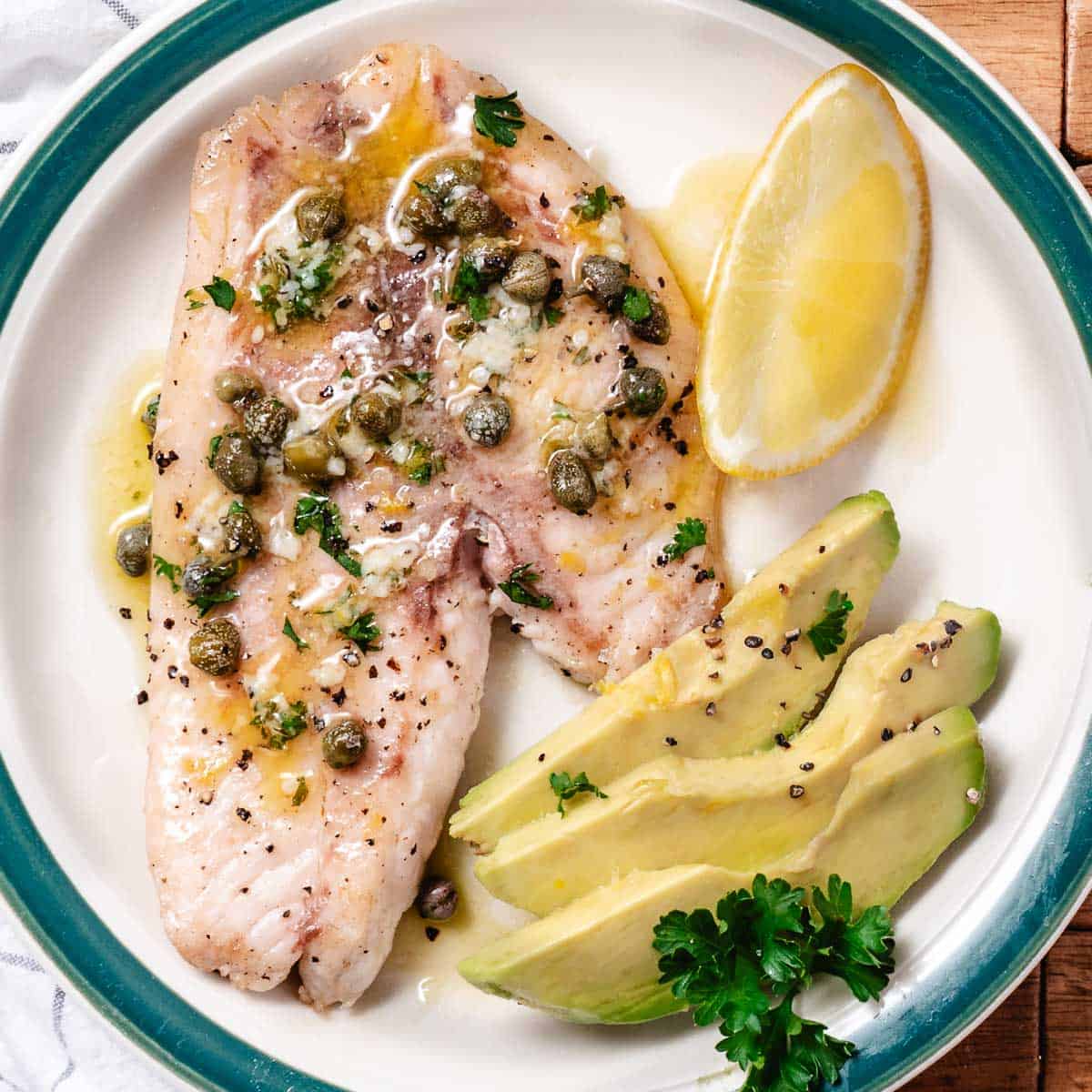 Pan-seared fish topped with lemon butter, capers, garlic, and parsley with a lemon wedge