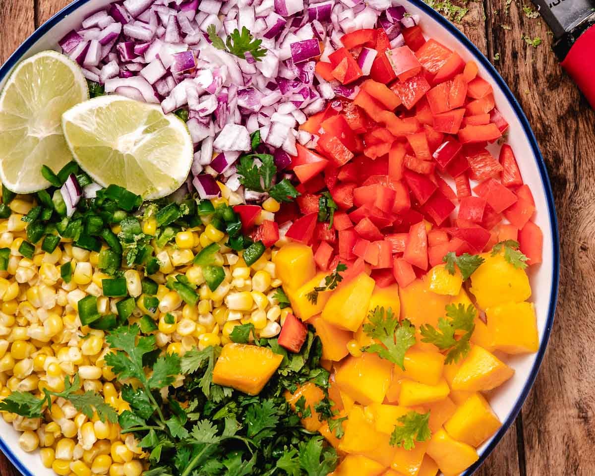 Corn mango salsa ingredients with fresh corn, mango, tomato, red onion, jalape&ntilde;o, cilantro, and lime.
