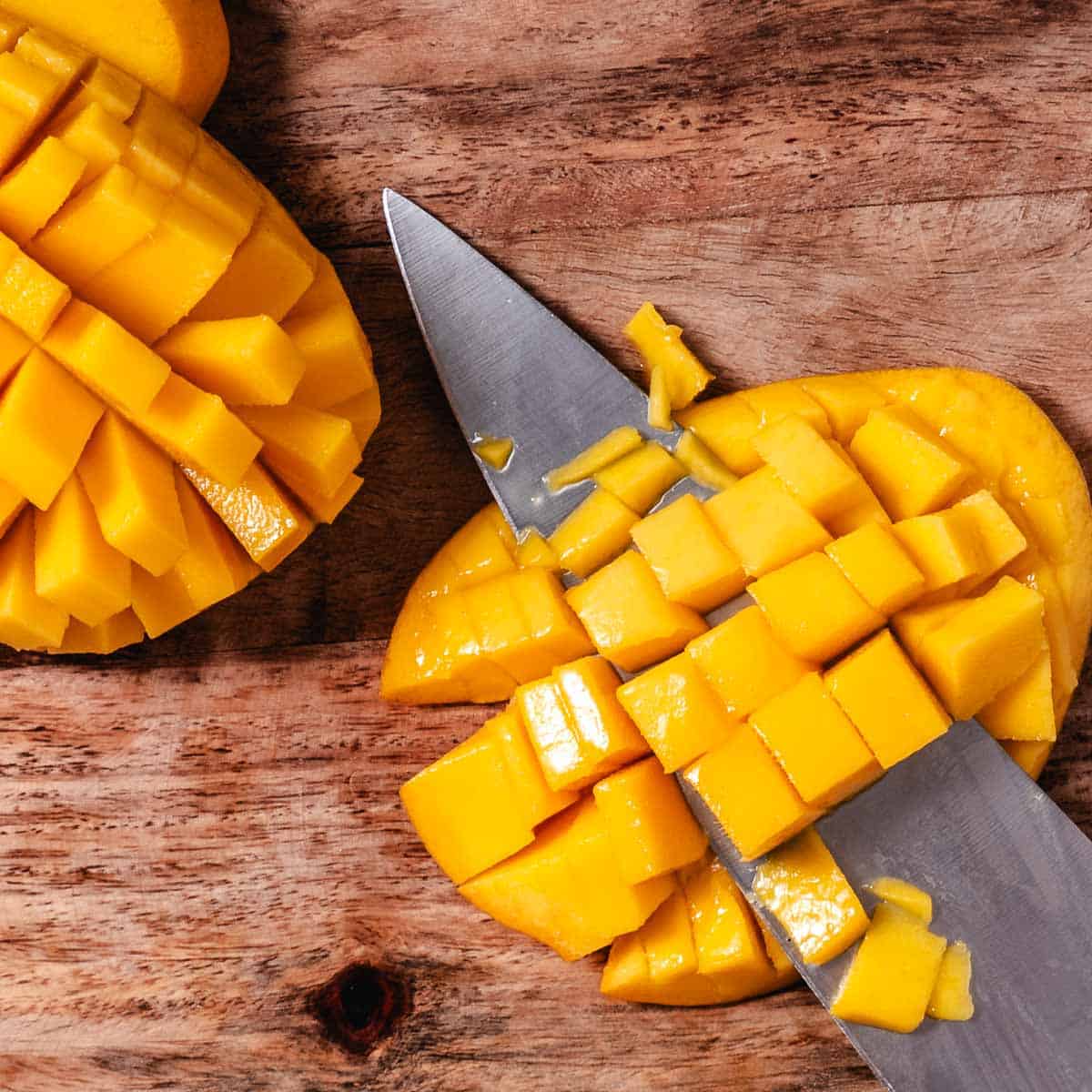 Fresh mango cut into cubes on a wooden cutting board with a knife.
