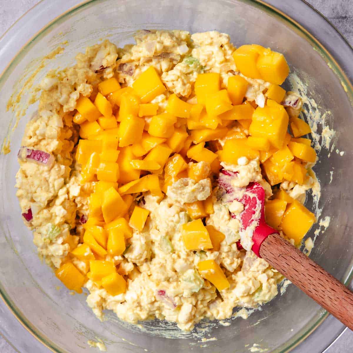 Mango being folded into egg salad with celery, red onion, and mayonnaise.