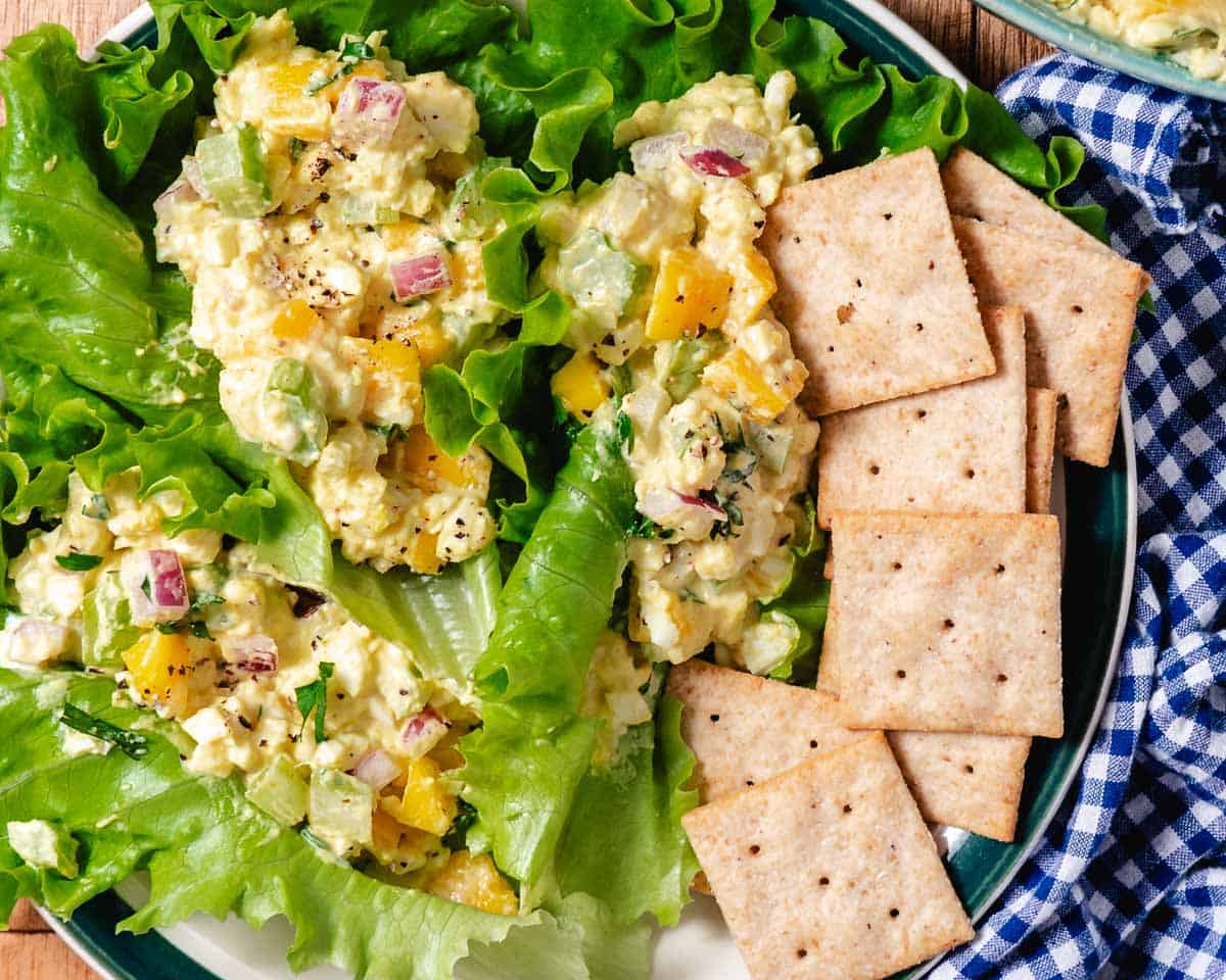 Mango egg salad served on green lettuce leaves with crackers on the side.