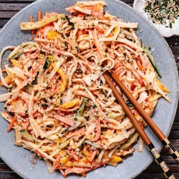 Mango kani salad with imitation crab, cucumber, carrot, mango, masago, and furikake served on a gray plate with chopsticks.