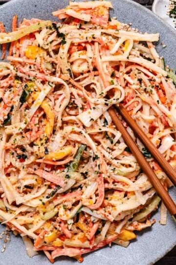 Mango kani salad with imitation crab, cucumber, carrot, mango, masago, and furikake served on a gray plate with chopsticks.
