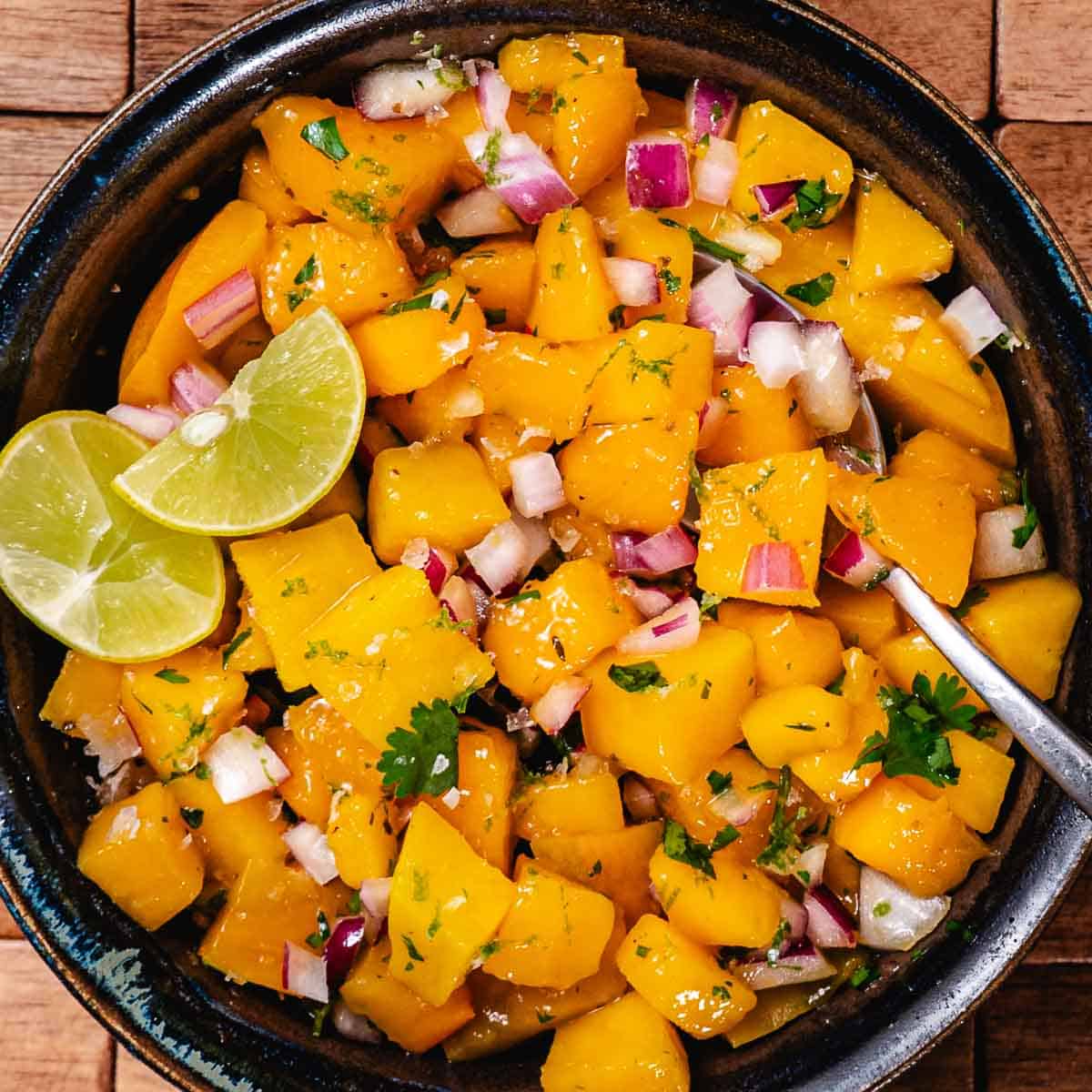 Mango salsa with red onion, cilantro, and fresh lime juice in a dark serving bowl