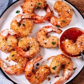 Gluten-free coconut shrimp served with sweet chili dipping sauce on a white plate.